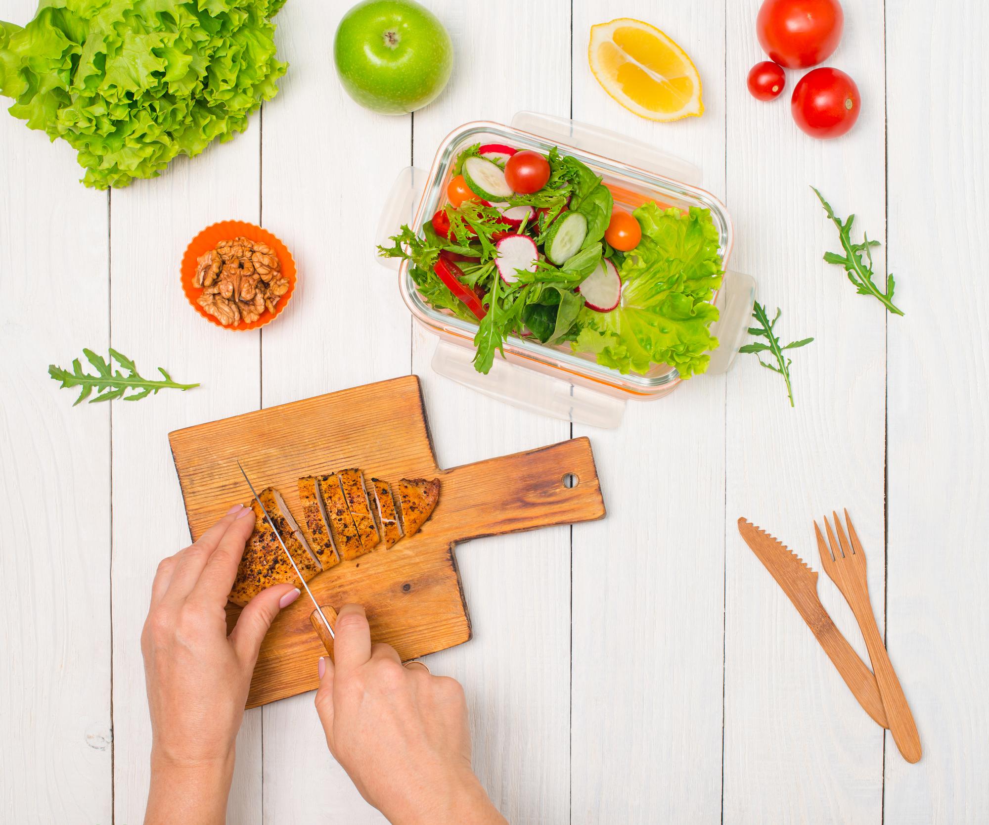 Hands arranging a fresh salad on a wooden board